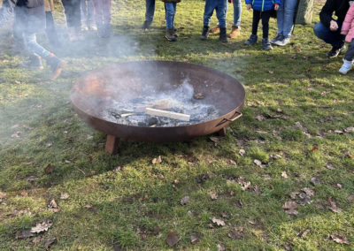 Feuerangebot 2026 - In einer Feuerschale wird ein Feuer gemacht. Um die Feuerschale herum stehen Kinder und Eltern.